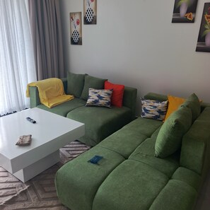 A green sofa with a white coffee table, a remote control, and a small bag on the table. - 1-bedroom apartment in perfect Nairobi with fitness room access (Nairobi)