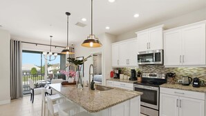 A modern kitchen with white cabinets, a granite countertop, stainless steel appliances, and a large island with bar stools. - Lakefront Luxury + Stunning Naples Sunsets (Naples)