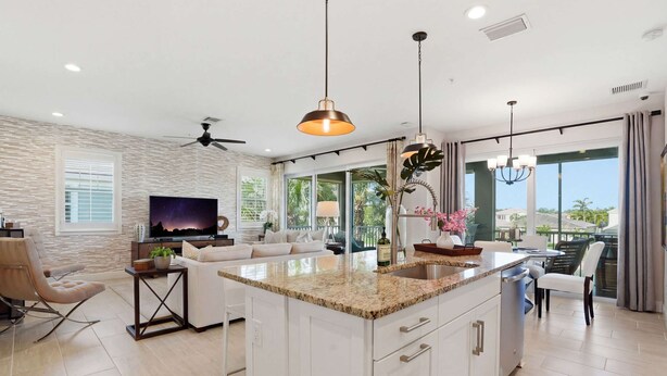 A modern kitchen with a central island, a dining area with a table and chairs, a living room with a sofa and TV, and large windows with a view. - Lakefront Luxury + Stunning Naples Sunsets (Naples)