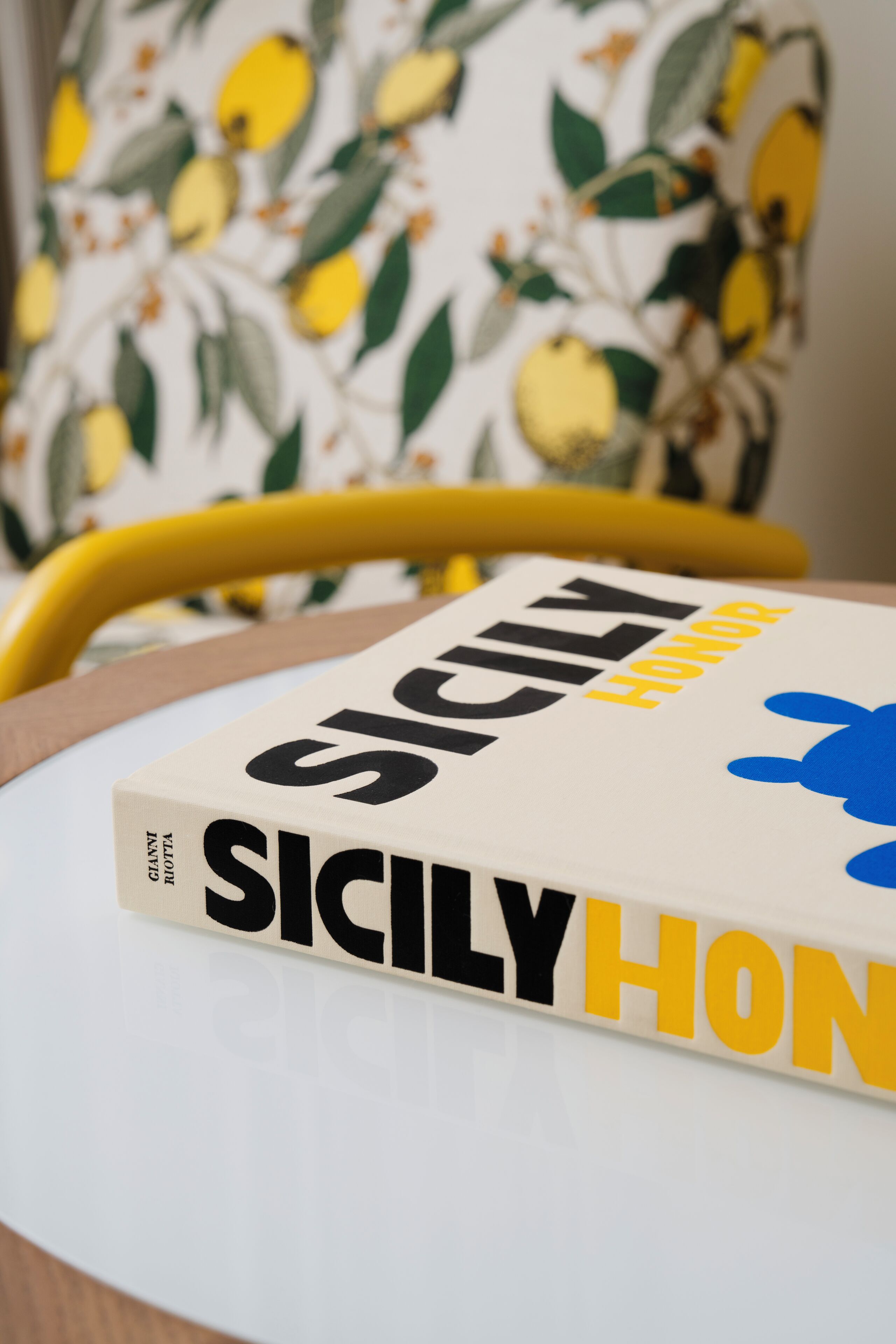 A book titled 'SICILY HONOR' on a table with a yellow chair in the background.