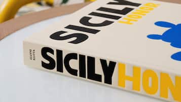 Un libro intitolato 'SICILY HONOR' su un tavolo, sullo sfondo una sedia gialla.