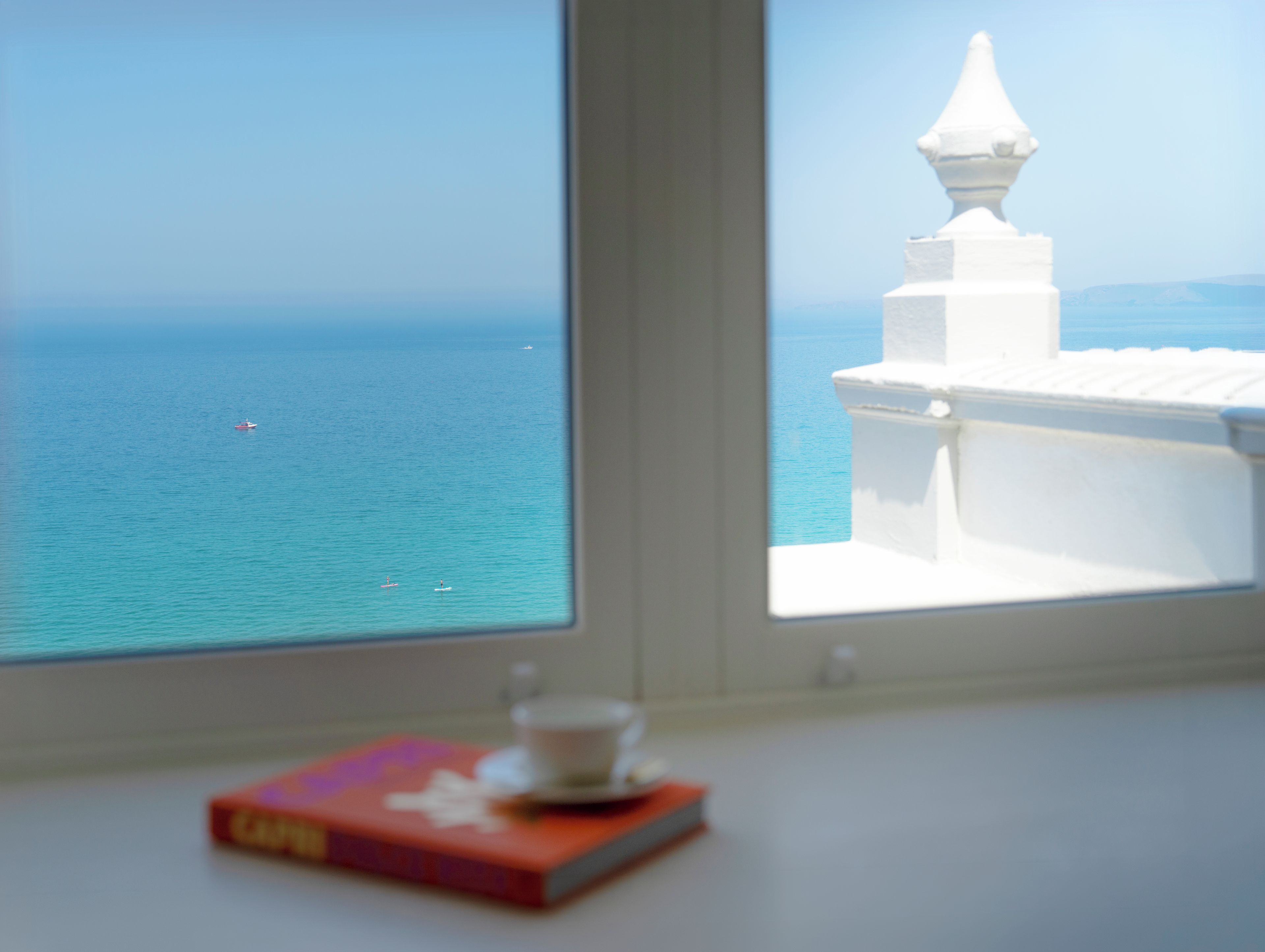 Vista del mare attraverso una finestra con balaustra bianca e un libro sul davanzale.