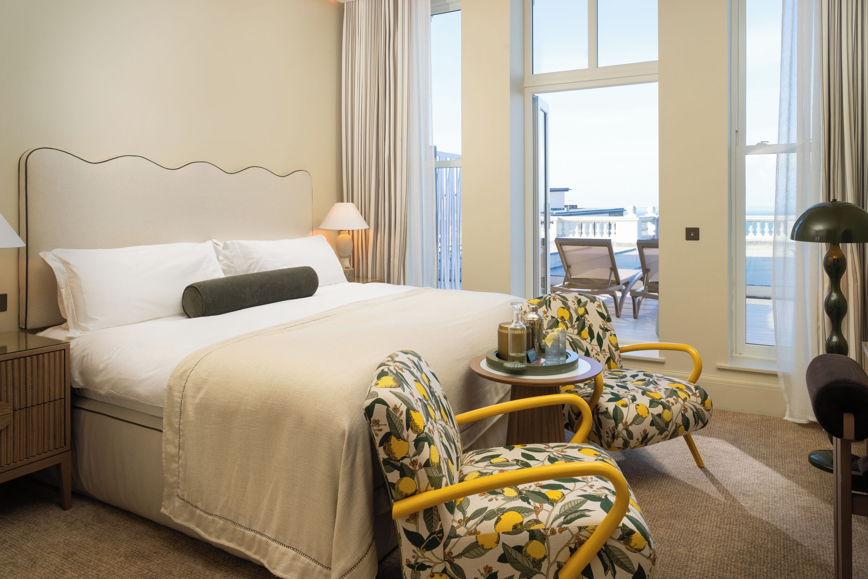 A hotel room with a bed, two chairs, a small table, and a view of the outside.
