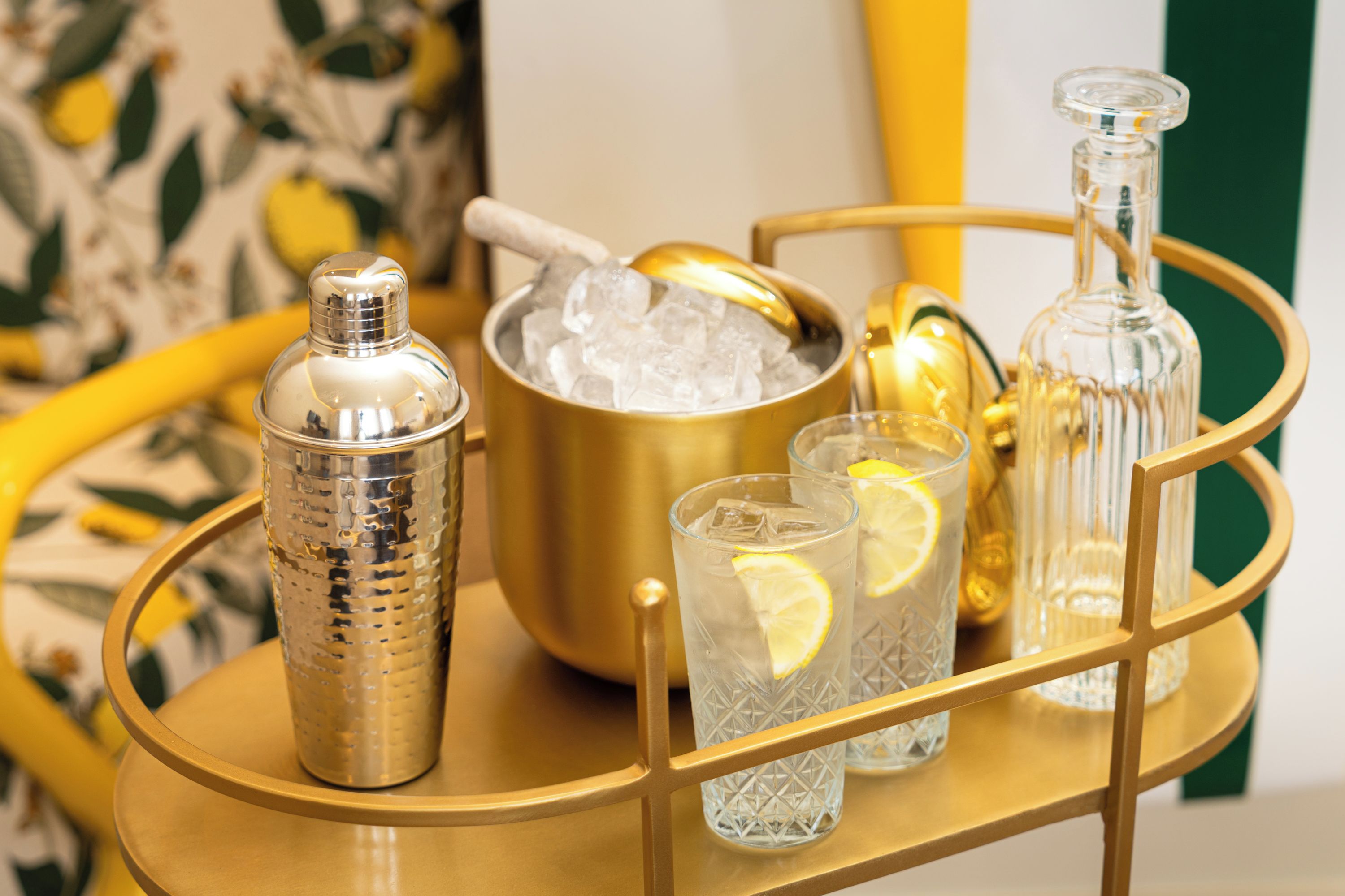 A bar setup with a cocktail shaker, a bucket of ice, and glasses with lemon slices.