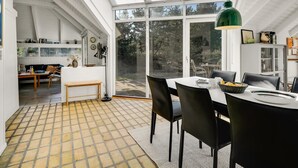 Moderni sisustus, jossa on ruokailutila, keittiö ja suuri lasiovi, joka johtaa puutarhaan.