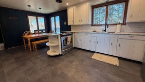Eine Küche mit weißen Schränken, einem eingebauten Backofen und einem Essbereich mit Holztisch und Stühlen.