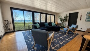 Ein geräumiges Wohnzimmer mit großem Fenster, einem blauen Teppich mit Muster und Holzboden.