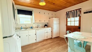 A kitchen with wooden cabinets, a white refrigerator, and a dining area with a table and chairs. - The Tinker Bell at Moody Beach- Turtle Unit 2 BR’s with partial ocean views (Wells)