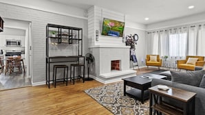 A modern living room with a fireplace, a dining area, and a kitchen visible through an open door.