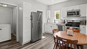 A modern kitchen with white cabinetry, stainless steel appliances, and a dining area with a wooden table and chairs.