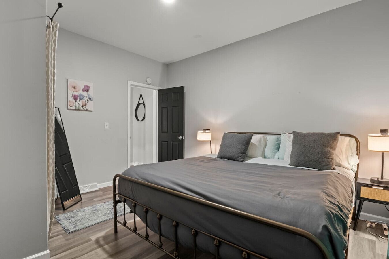 Una camera da letto con un letto, lampade sui comodini, una porta e un quadro appeso al muro.