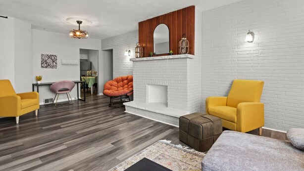 A modern living room with a fireplace, two yellow armchairs, a round orange chair, and a dining area in the background.