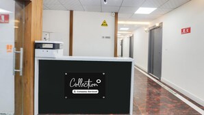 A reception desk with a sign reading 'Collection & Company Serviced,' a fire exit sign, and a warning sign on the wall. - Classic With Balconyjr inn (Lucknow)