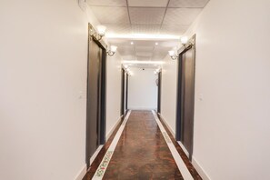 A long, narrow hallway with white walls, dark doors, and a patterned floor.
