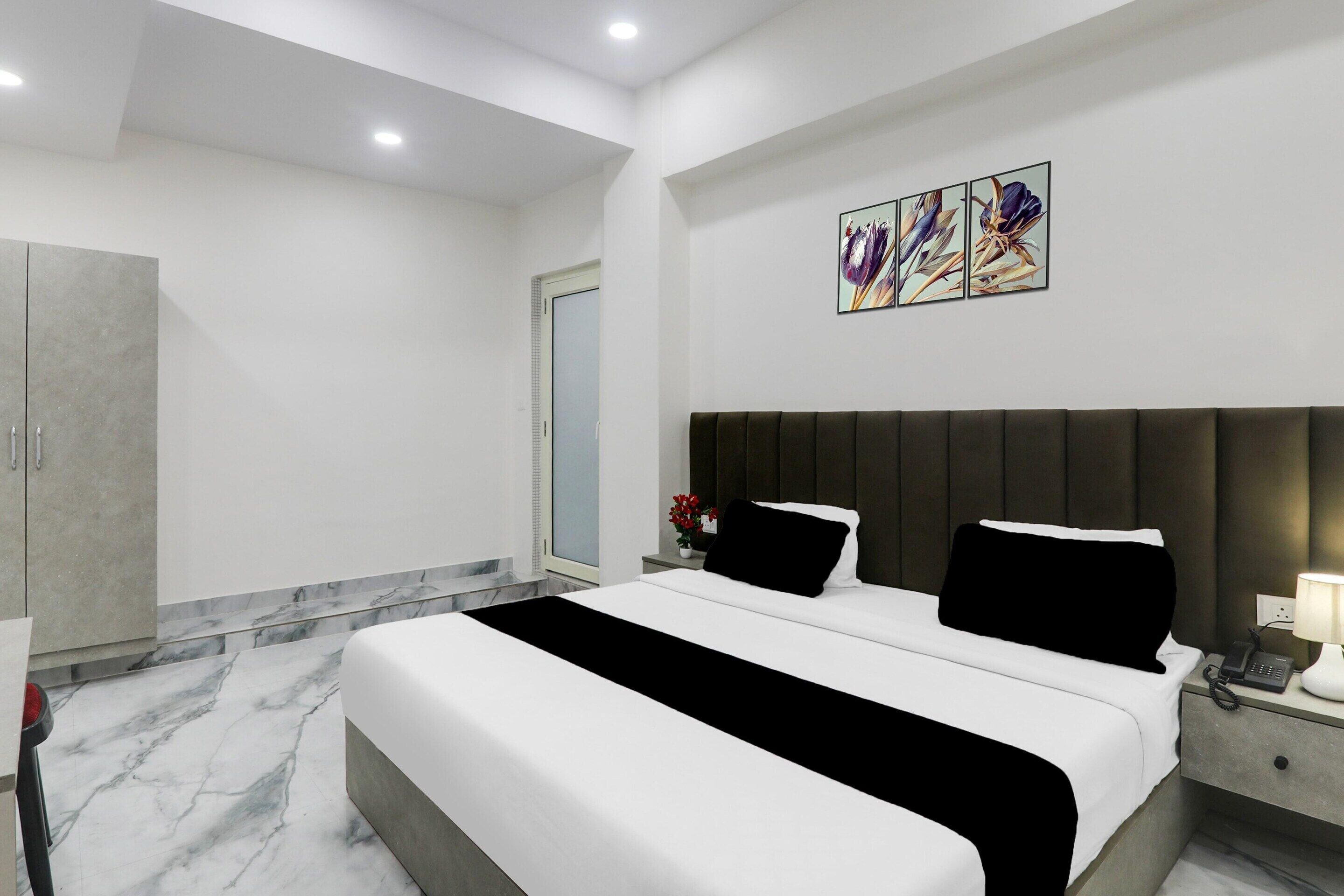 Una habitació d'hotel moderna amb un llit gran, un armari, una tauleta de nit amb una làmpada i una obra d'art penjada a la paret.