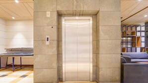 Un ascenseur dans un hall d’entrée avec un sol à carreaux, un canapé et une bibliothèque.