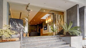L’entrée d’un hôtel, avec une façade en verre, un comptoir d’accueil et un escalier menant au hall d’entrée.