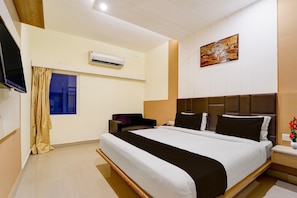 A hotel room with a bed, a flat-screen TV, an air conditioning unit, a window with curtains, and a painting on the wall. - Townhouse Dindigul Rock Fort (Thindukkal)