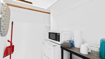 A compact kitchen with a microwave, a kettle, and a small table with cups and a bottle.