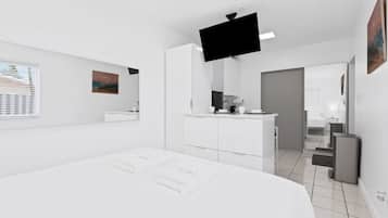 Ein modernes Hotelzimmer mit einem großen Bett, einem Flachbildfernseher, einer kleinen Küchenzeile und einem durch eine geöffnete Tür einsehbaren Badezimmer.