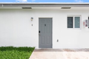 A building with a gray door marked with the letter 'K', a small window, and a fire alarm on the right. - Private modern studio w/ pool - Steps to the beach (Deerfield Beach)