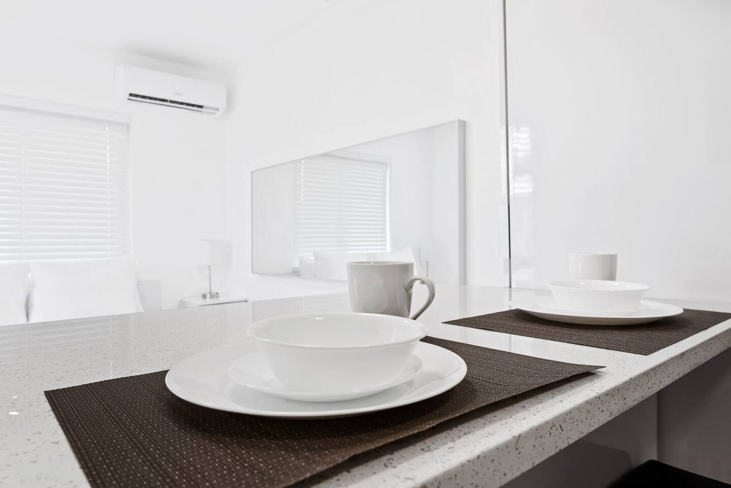 Un baño moderno con un espejo grande, una encimera con un lavabo y una taza, y un ventanal con persianas.