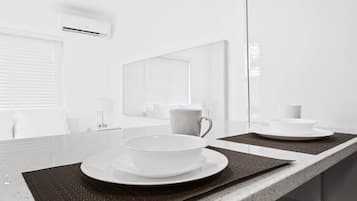 A modern bathroom with a large mirror, a countertop with a bowl and cup, and a window with blinds.