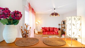 Una sala de estar con sofá, una planta decorativa, una lámpara y una estantería de pared.