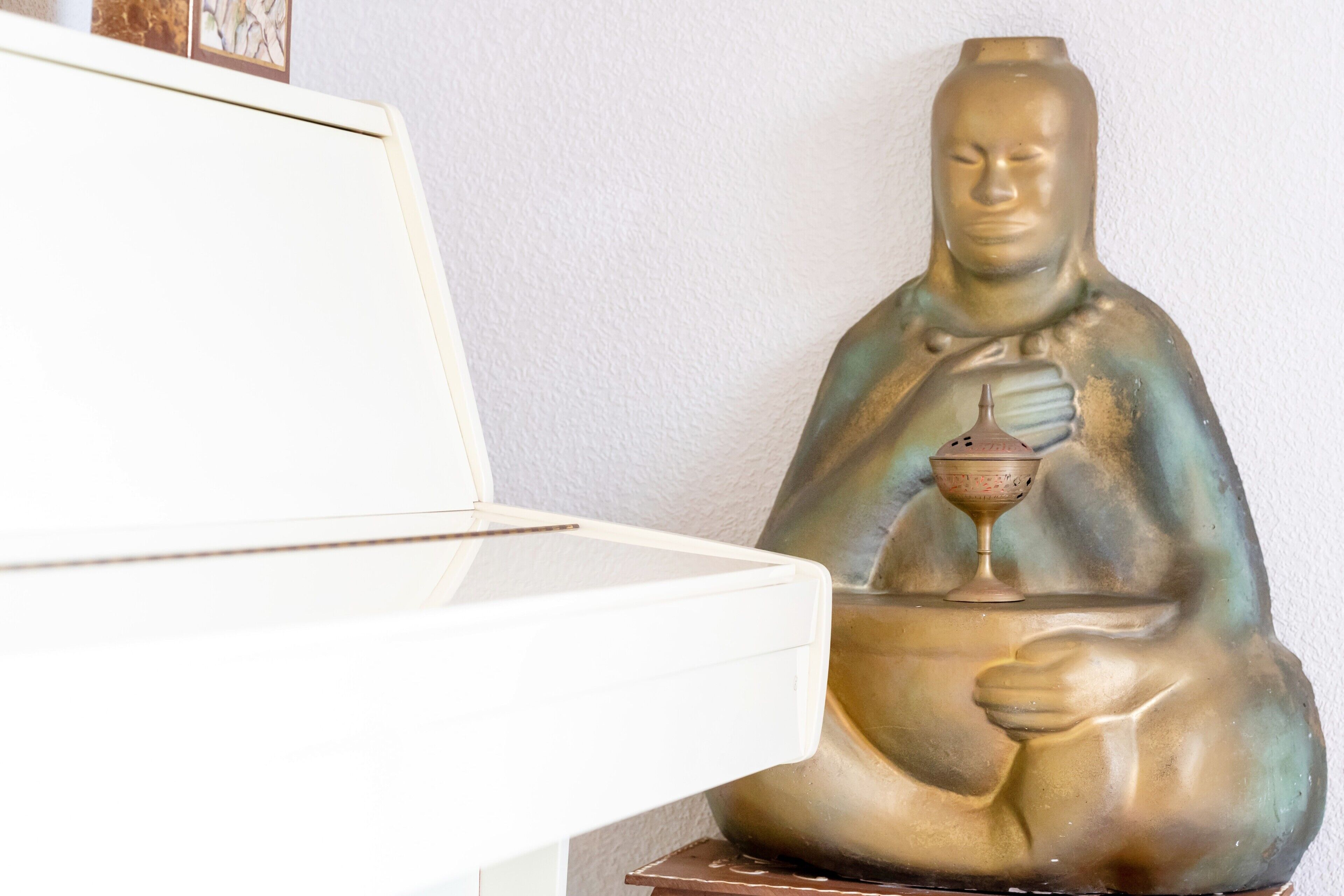 Een standbeeld van een zittend figuur met een beker, geplaatst op een tafel naast een witte kast.