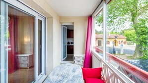 Un balcón con vista a un árbol, una puerta que da a una habitación y una mesa con un cojín.