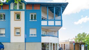 Un edificio de dos pisos con fachada azul y beige, un balcón y un acceso de vidrio.