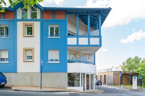 Un immeuble de deux étages avec une façade bleue et beige, un balcon et une entrée en verre.