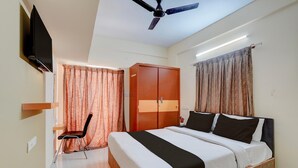 A hotel room with a bed, a chair, a wardrobe, a television, and a ceiling fan. - Saver Singlehotel O Channasandra (Bengaluru)