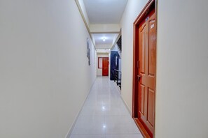 Un couloir avec un sol carrelé, une porte en bois et, au loin, une porte rouge.