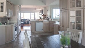 A spacious kitchen with white cabinetry, a dishwasher, and a dining area with a wooden table and chairs. - On The Rocks • Waterfront Retreat Near Point Pelee (Leamington)