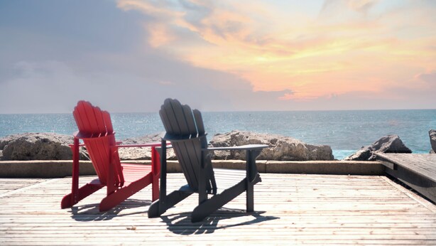 Two Adirondack chairs on a wooden deck with a view of the ocean and rocks in the background. - On The Rocks • Waterfront Retreat Near Point Pelee (Leamington)