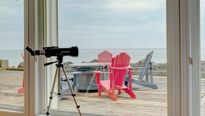 A telescope on a tripod, a red Adirondack chair, and a table on a wooden deck with a view of the sea. - On The Rocks • Waterfront Retreat Near Point Pelee (Leamington)