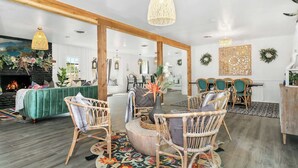 Un salon spacieux doté d’une cheminée, d’un canapé vert, de fauteuils en osier et d’un coin repas avec une table et des chaises.