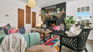 Un salon chaleureux avec une cheminée en pierre, un canapé, un fauteuil et un tapis aux couleurs vives.