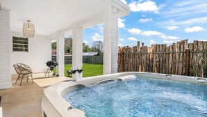 Un bain à remous avec une terrasse en bois, un barbecue et deux fauteuils en osier.