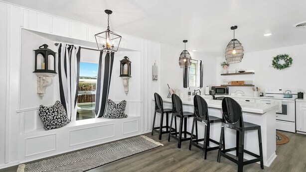 Une cuisine moderne avec des meubles blancs, un îlot central doté de tabourets de bar, un éclairage suspendu et une vue dégagée grâce à de grandes fenêtres.