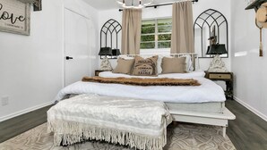 Une chambre à coucher comprenant un lit, un lustre, deux tables de chevet, une fenêtre avec des rideaux et un élément décoratif mural.
