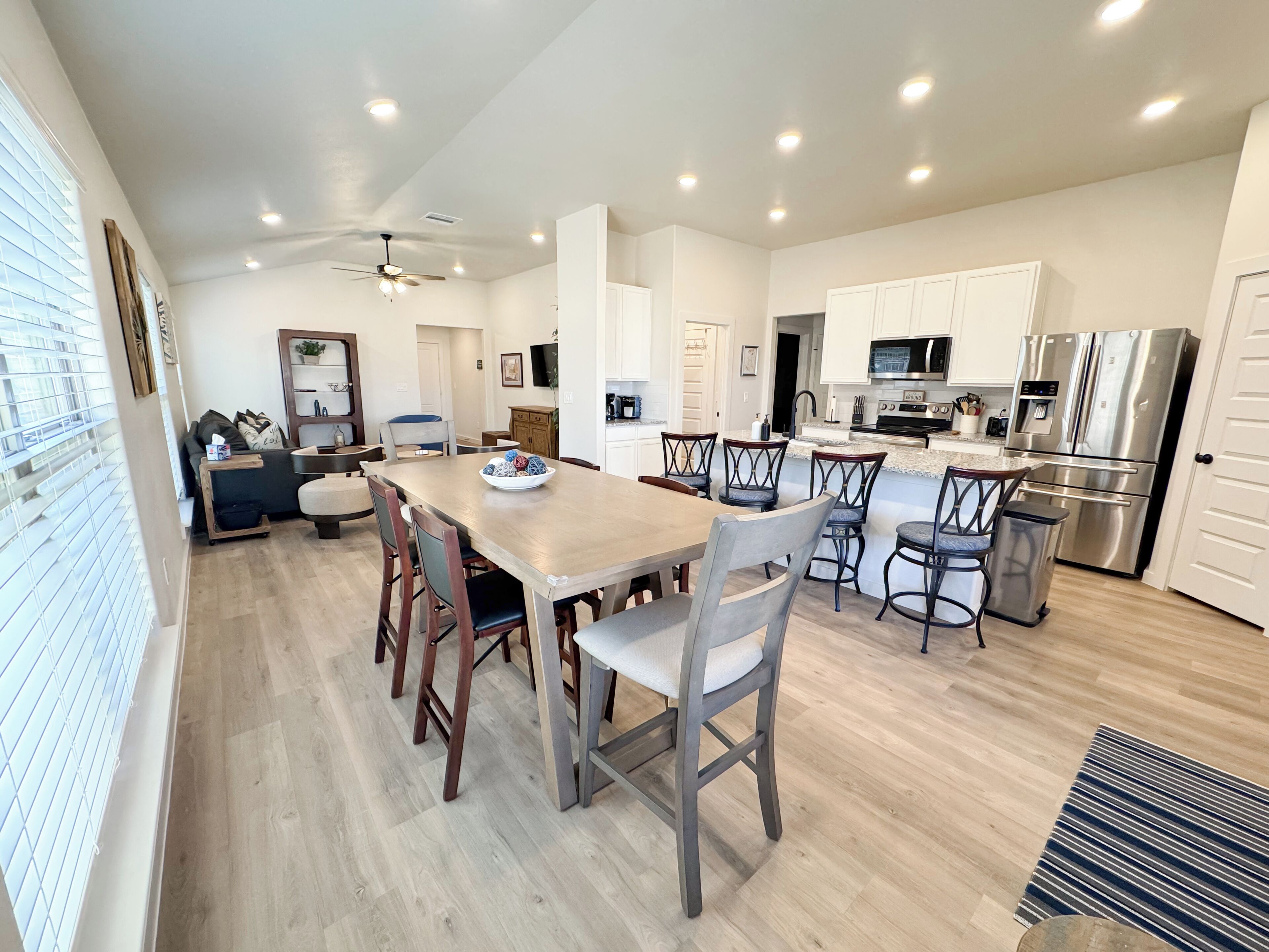 A modern kitchen with white cabinets, stainless steel appliances, and a dining area with wooden chairs and a central island.