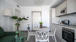 Uma cozinha moderna com armários brancos, uma área de jantar com mesa e cadeiras redondas, e um sofá verde.
