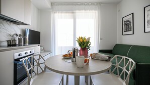 Uma cozinha moderna com uma mesa de jantar, cadeiras, um sofá verde e uma janela com cortinas.