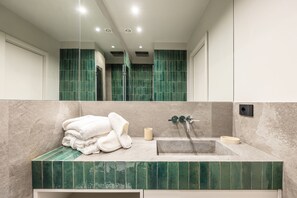 Ein Badezimmer mit Waschbecken, Spiegel, grünen Fliesen und Handtüchern.