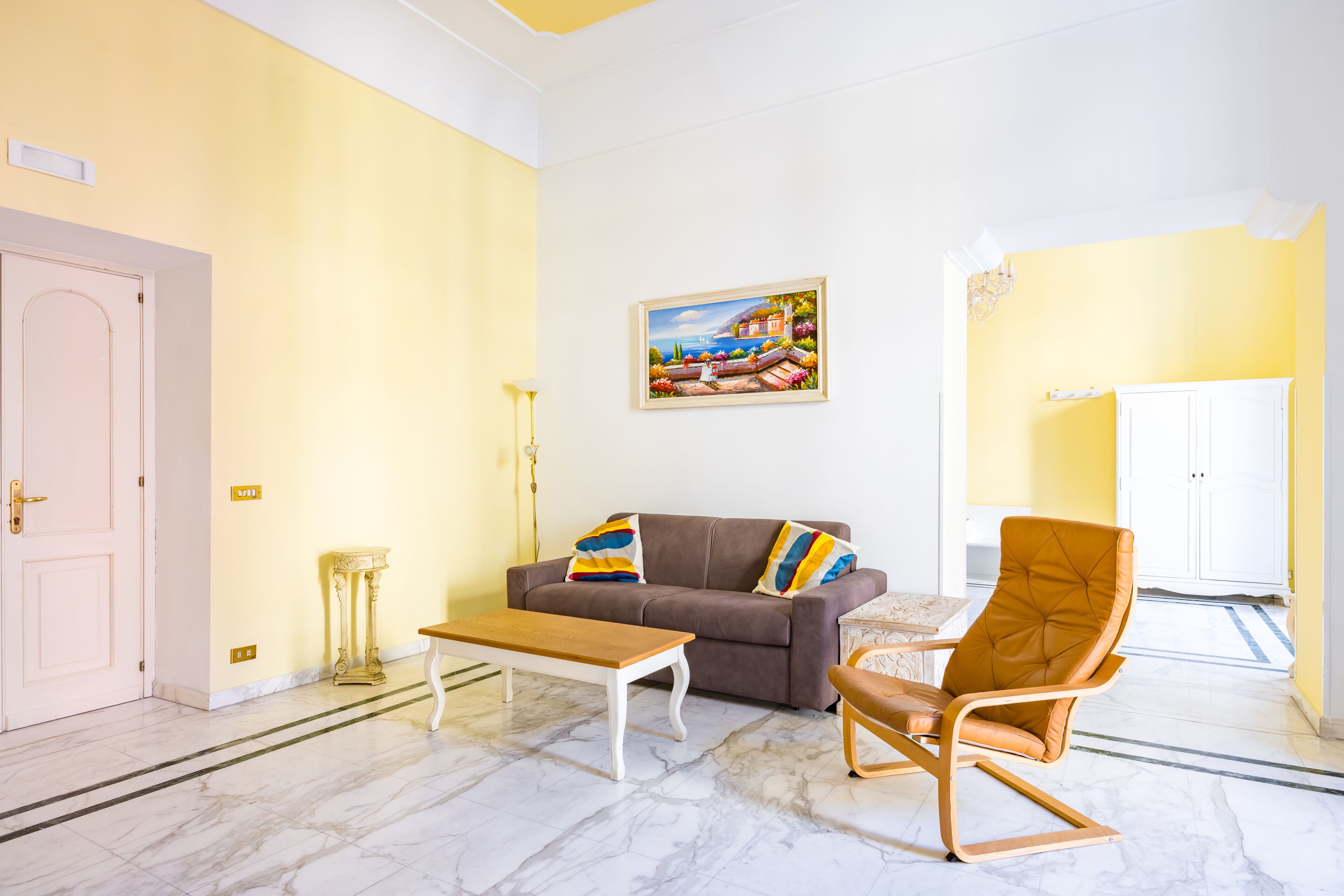 A living room with a sofa, a chair, a coffee table, a painting, and a door.