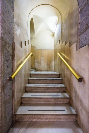 Un escalier aux marches de marbre et aux rampes dorées, menant à un plafond en arc de cercle.