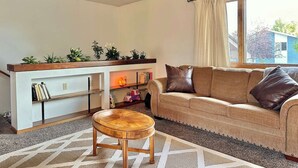 A living room with a sofa, a wooden coffee table, a bookshelf, and a window with curtains.