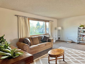 A living room with a sofa, a round wooden table, a floor lamp, and a bookshelf.